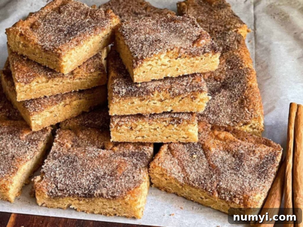 Effortlessly Chewy Snickerdoodle Bars 2 Snickerdoodle Bars stacked on a wooden cutting board, showcasing their golden-brown edges and cinnamon sugar topping.