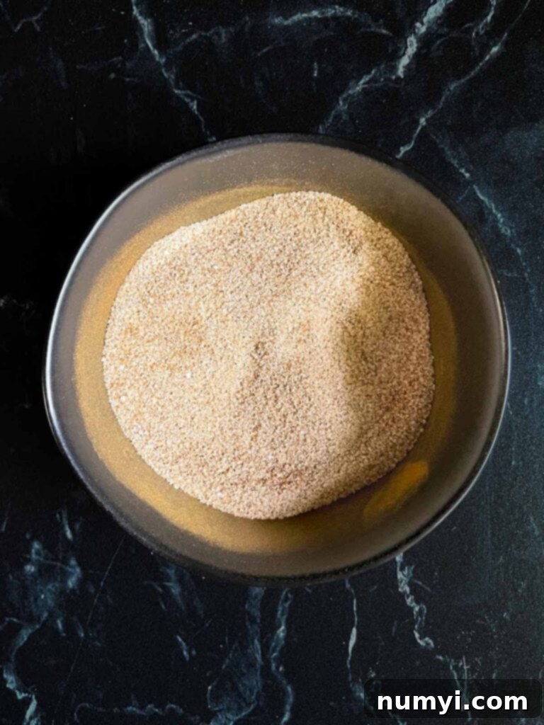 Effortlessly Chewy Snickerdoodle Bars 8 Cinnamon sugar mixture for Snickerdoodle Bars in a small bowl on a dark surface, ready for sprinkling.