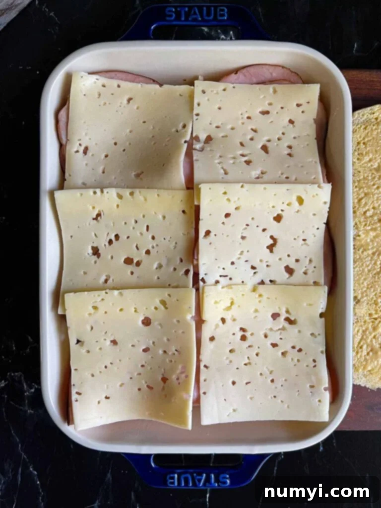 Whip Up Easy Monte Cristo Sliders for Your Next Bash 11 Swiss layered over slider rolls in a baking dish.