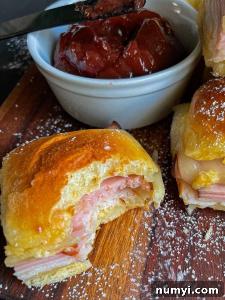 Whip Up Easy Monte Cristo Sliders for Your Next Bash 17 Monte Cristo sliders stacked up on a dark cutting board, one has a bite out of it.