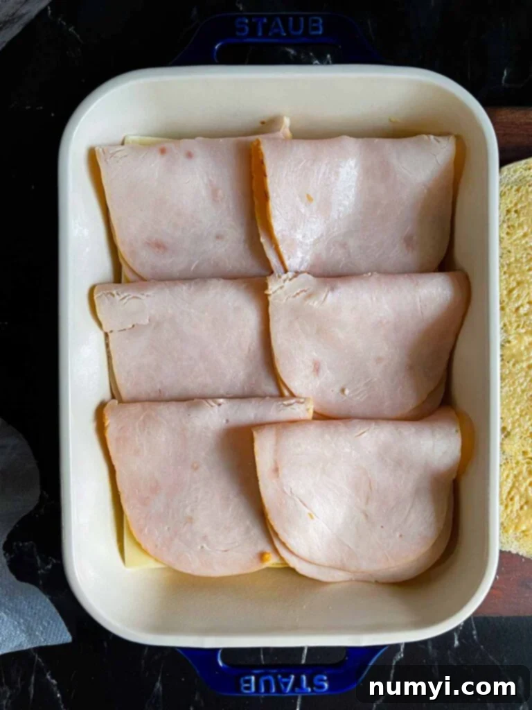 Whip Up Easy Monte Cristo Sliders for Your Next Bash 9 Turkey layered over slider rolls in a baking dish.