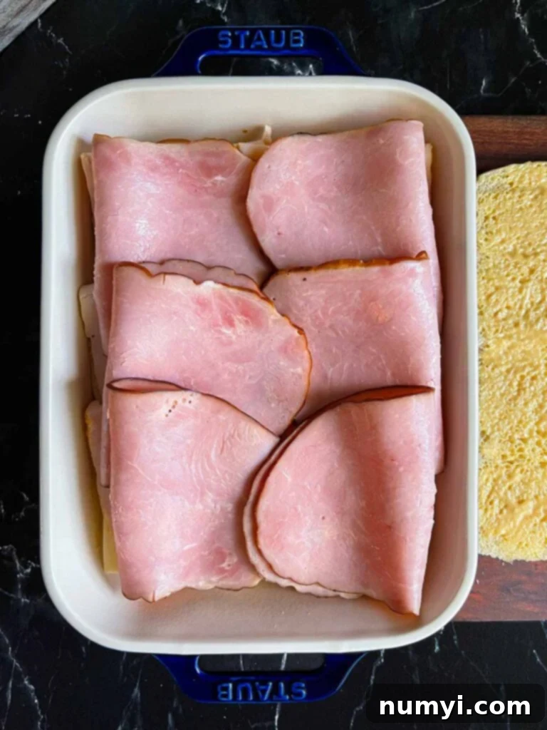 Whip Up Easy Monte Cristo Sliders for Your Next Bash 10 Ham layered over slider rolls in a baking dish.