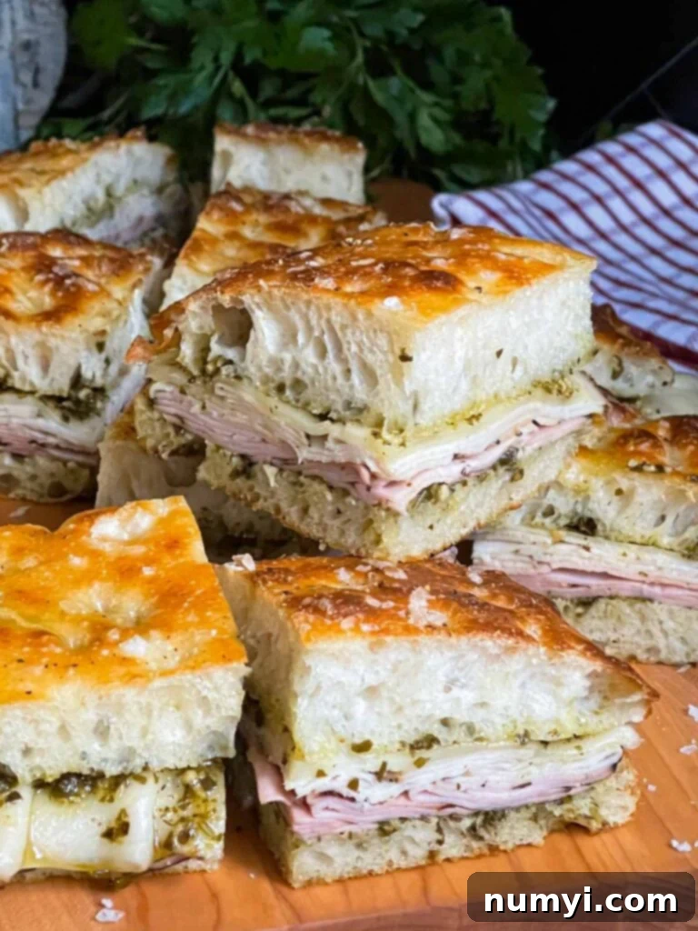 Freshly sliced pesto focaccia sandwiches arranged neatly on a rustic wooden cutting board, showcasing their vibrant layers and golden focaccia.