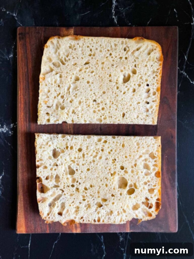 A freshly baked focaccia bread, perfectly sliced in half horizontally, revealing its soft interior, ready for fillings.