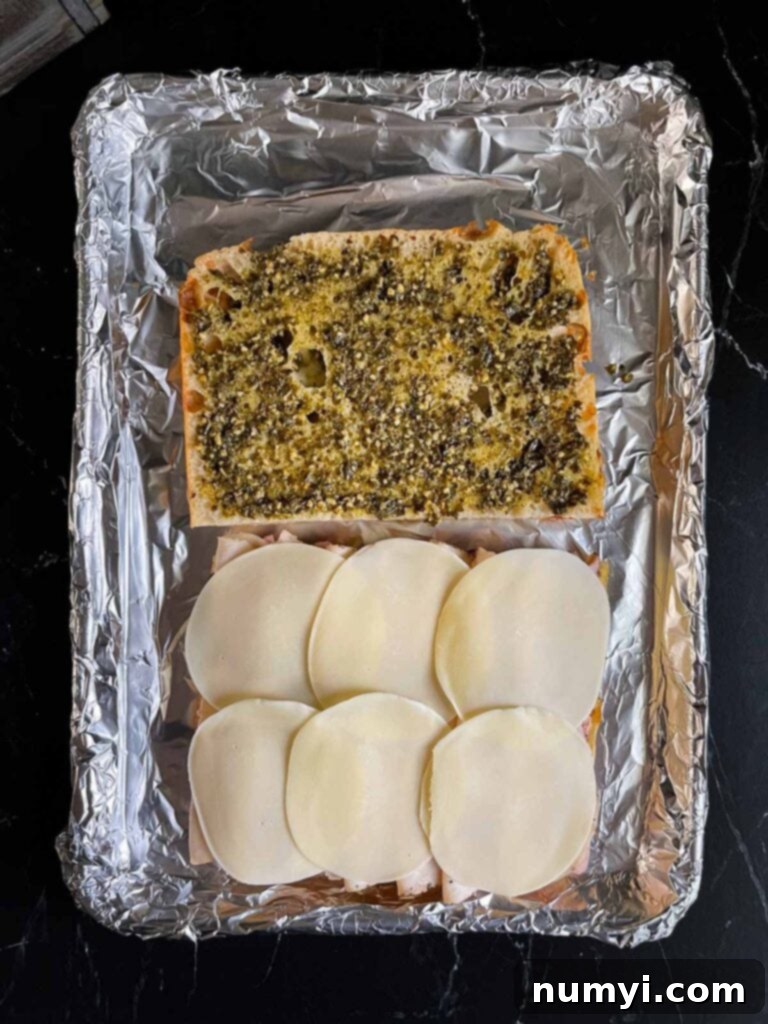 The focaccia sandwich layers continue with provolone cheese being added over the turkey and ham, preparing for the top layer.