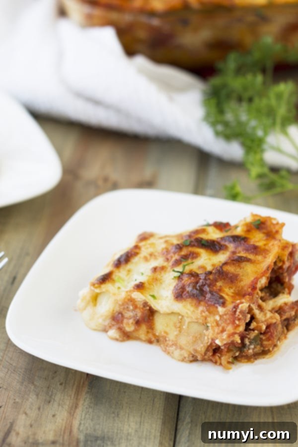 A perfectly portioned square of Five Cheese No-Boil Lasagna on a white plate, showcasing its distinct, delicious layers of pasta, meat sauce, and melted cheese, ready to be enjoyed.
