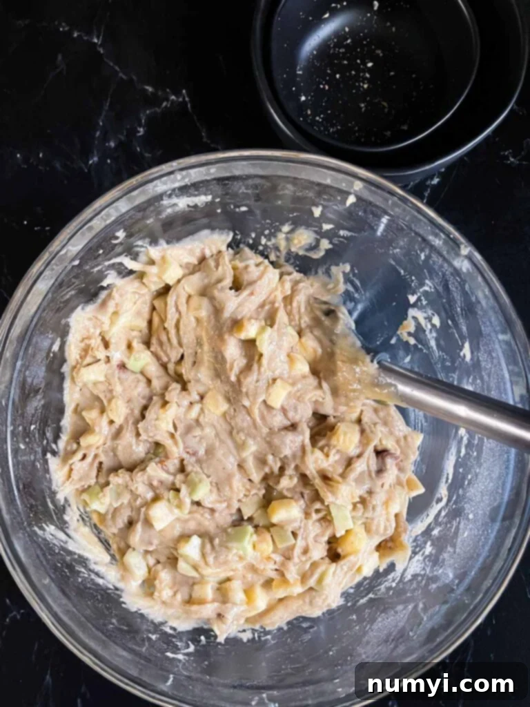 Apple Dapple Cake batter mixed in a glass mixing bowl on a dark suface.