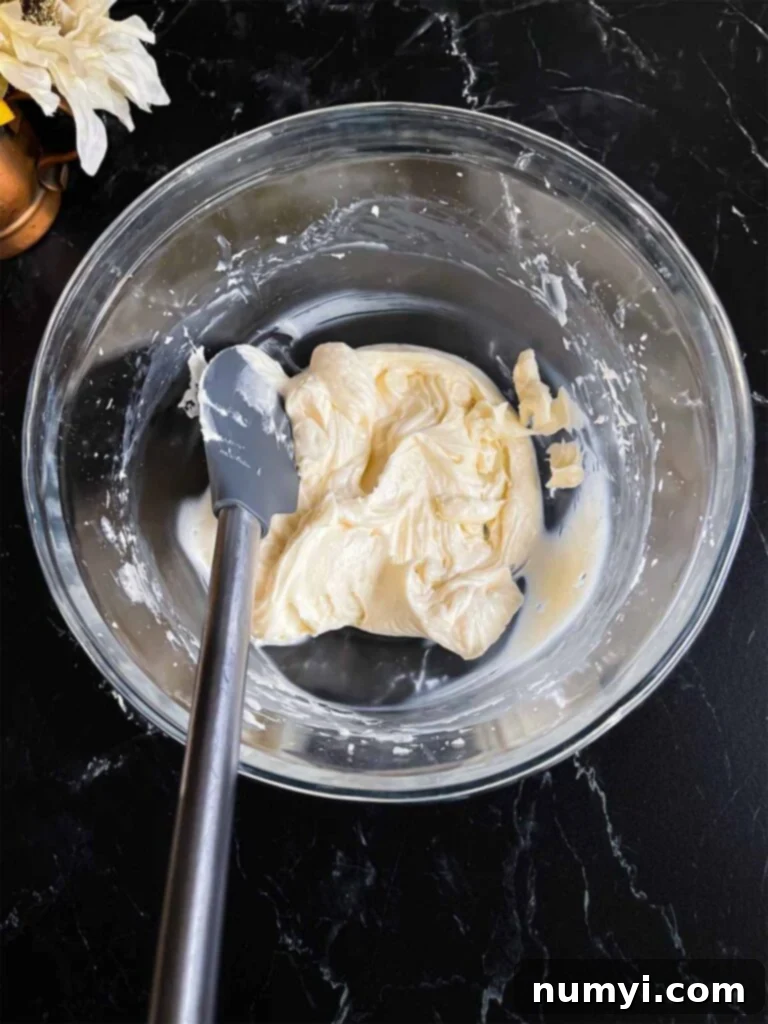 Spiced Sweet Potato Cake 12 Softened cream cheese in a glass mixing bowl on a dark surface.