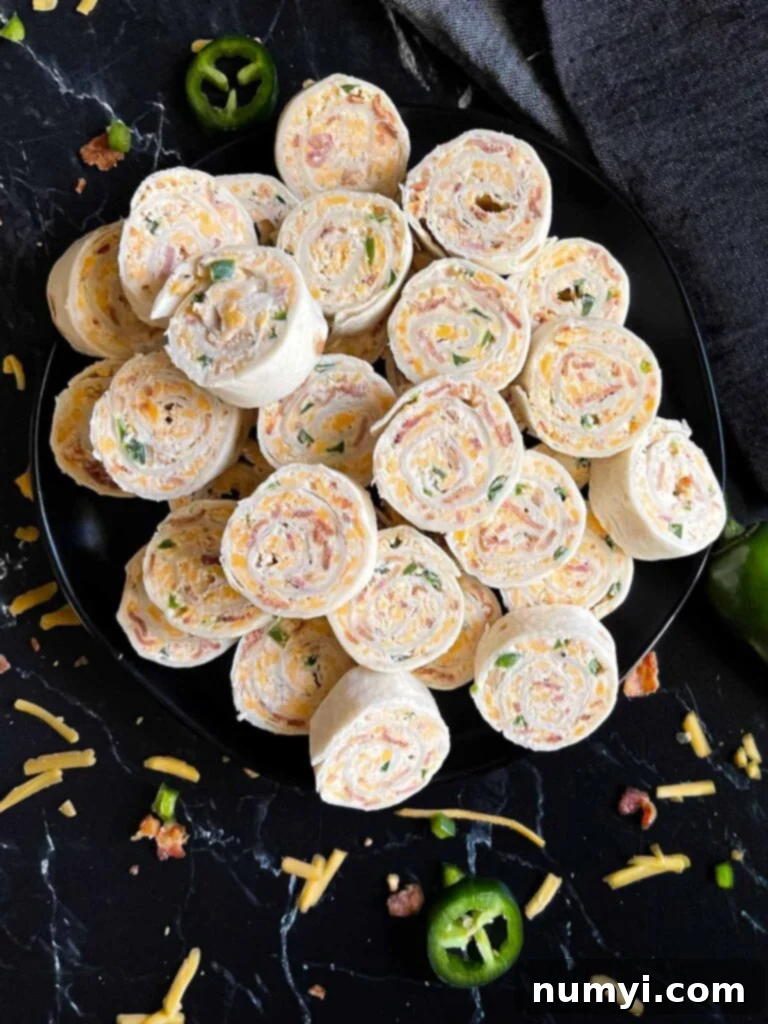 Jalapeno popper pinwheels on a dark plate on a dark surface.