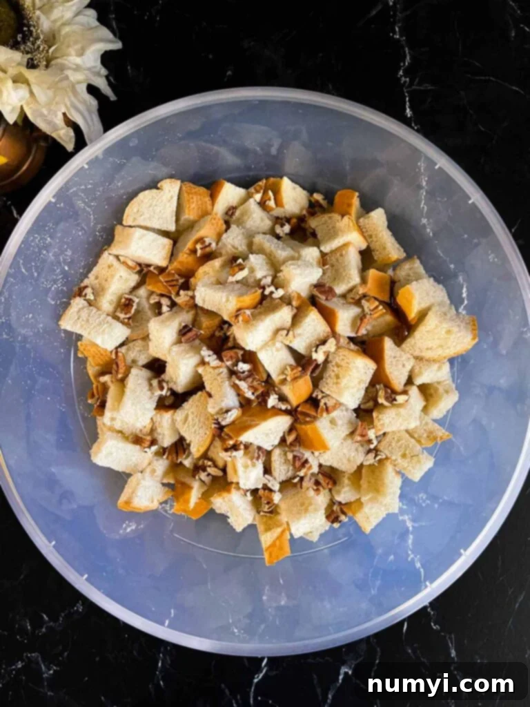 Salted Caramel Swirl Pumpkin Bread Pudding 5 Large bowl filled with 1-inch bread cubes and scattered toasted pecans, ready for the custard, on a dark countertop.