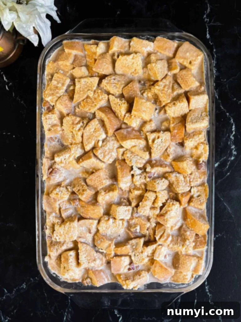 Salted Caramel Swirl Pumpkin Bread Pudding 8 Unbaked pumpkin bread pudding, perfectly soaked in custard, arranged in a buttered 9x13 inch baking dish, ready for refrigeration and baking, on a dark surface.
