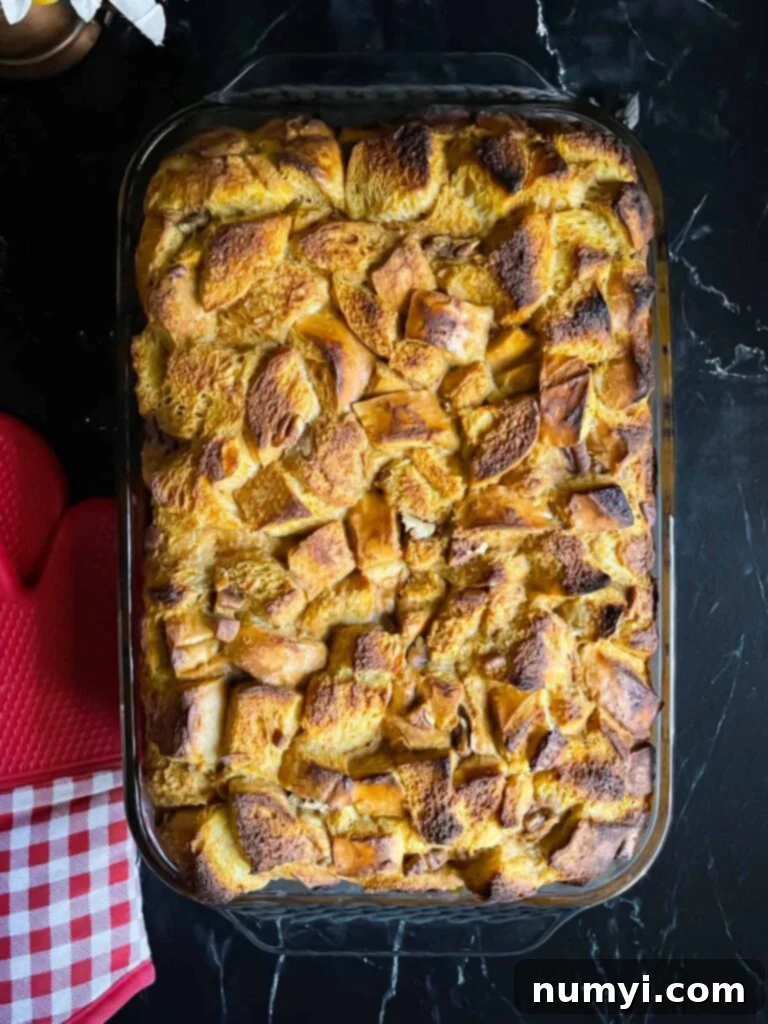 Salted Caramel Swirl Pumpkin Bread Pudding 9 Freshly baked pumpkin bread pudding, puffed and golden brown, in a 9x13 inch baking pan, cooling on a dark surface.
