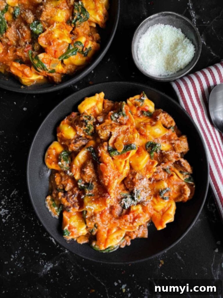 Cheese tortellini with sausage and spinach in a dark bowl on a dark surface.