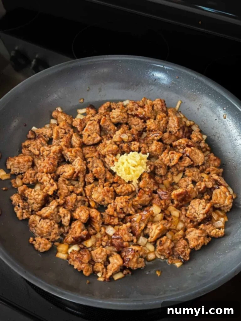Garlic added to browned italian sausage in a skillet.
