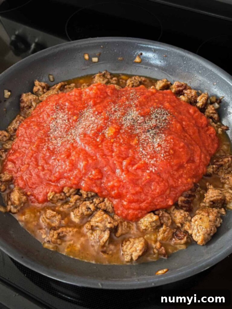 Crushed tomatoes added to italian sausage in a skillet.