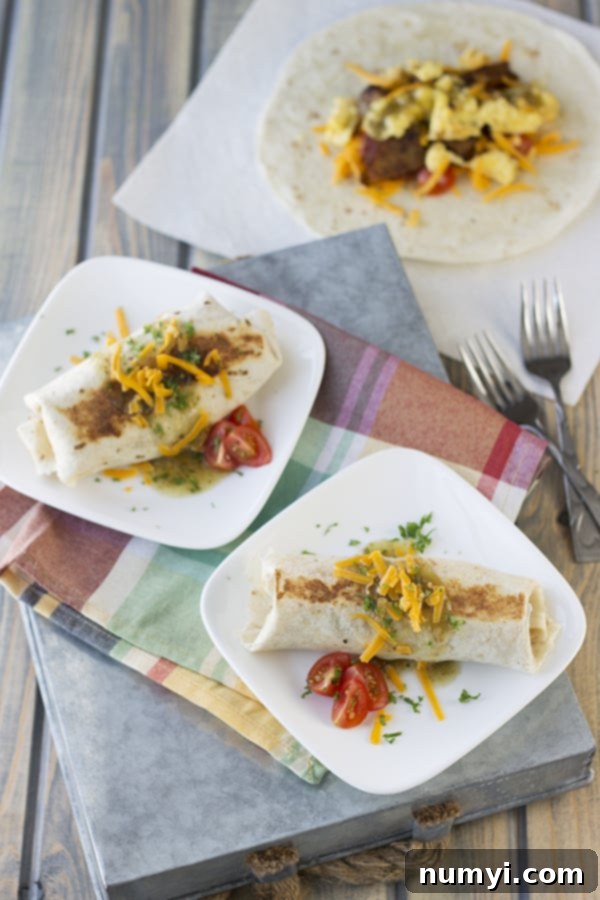 Grab-and-Go Breakfast Burritos 2 Two white plates each holding a perfectly wrapped breakfast burrito, garnished with fresh cheese, salsa, tomatoes, and herbs, ready to be enjoyed.
