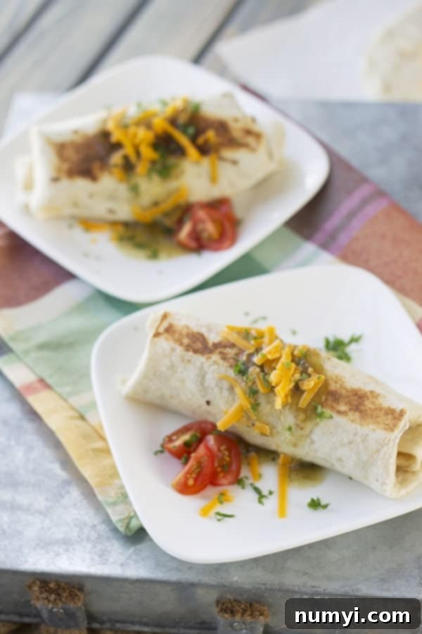 Grab-and-Go Breakfast Burritos 4 Two white plates on a colorful striped cloth, each presenting a perfectly golden-brown meal prep breakfast burrito, ready for serving.