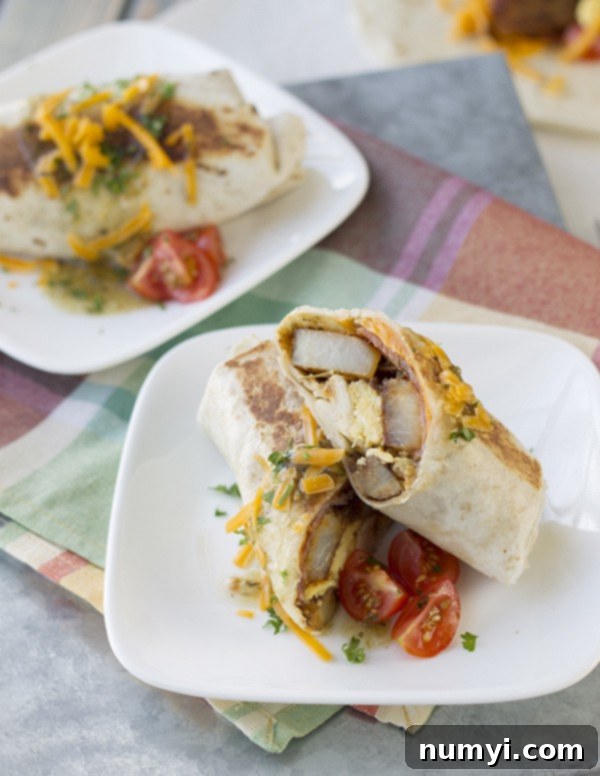 Grab-and-Go Breakfast Burritos 5 Two white plates with breakfast burritos, one cut in half revealing the savory layers of potatoes, eggs, bacon, and cheese inside.