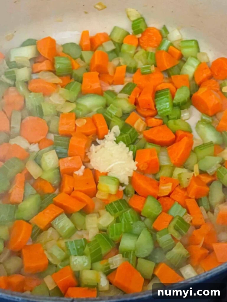 Velvety Potato Corn Chowder with Crispy Bacon 6 Garlic being added to onions, celery, and carrots in a dutch oven.
