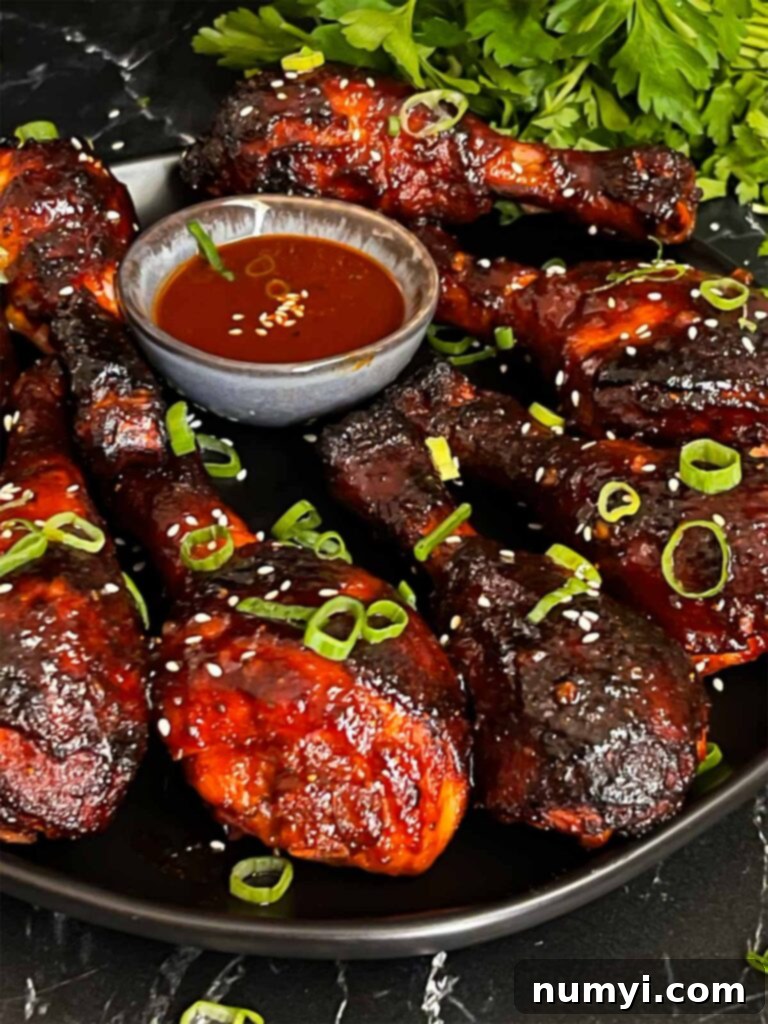 Plated smoked gochujang chicken legs, garnished with green onions and sesame seeds, ready to be enjoyed.