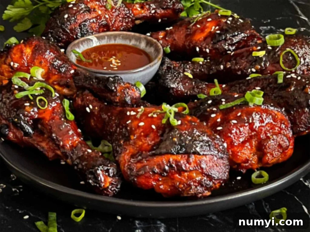 Close-up of smoked gochujang chicken legs garnished with fresh cilantro and sesame seeds on a dark plate.