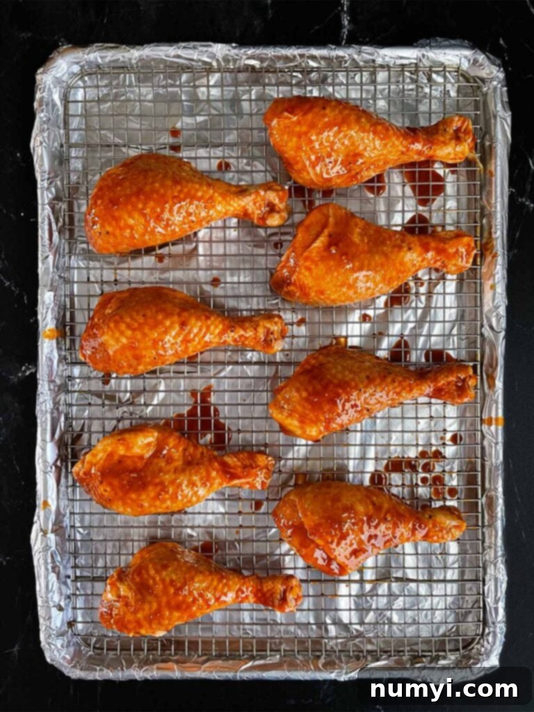 Marinated chicken legs resting on a cooling rack over a foil-lined baking sheet, prepared for smoking.