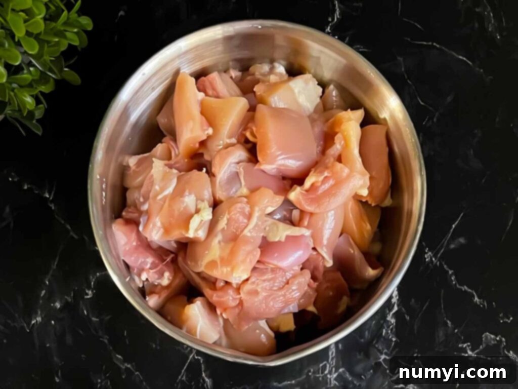 Cubed chicken thighs in a stainless steel bowl on a dark surface.