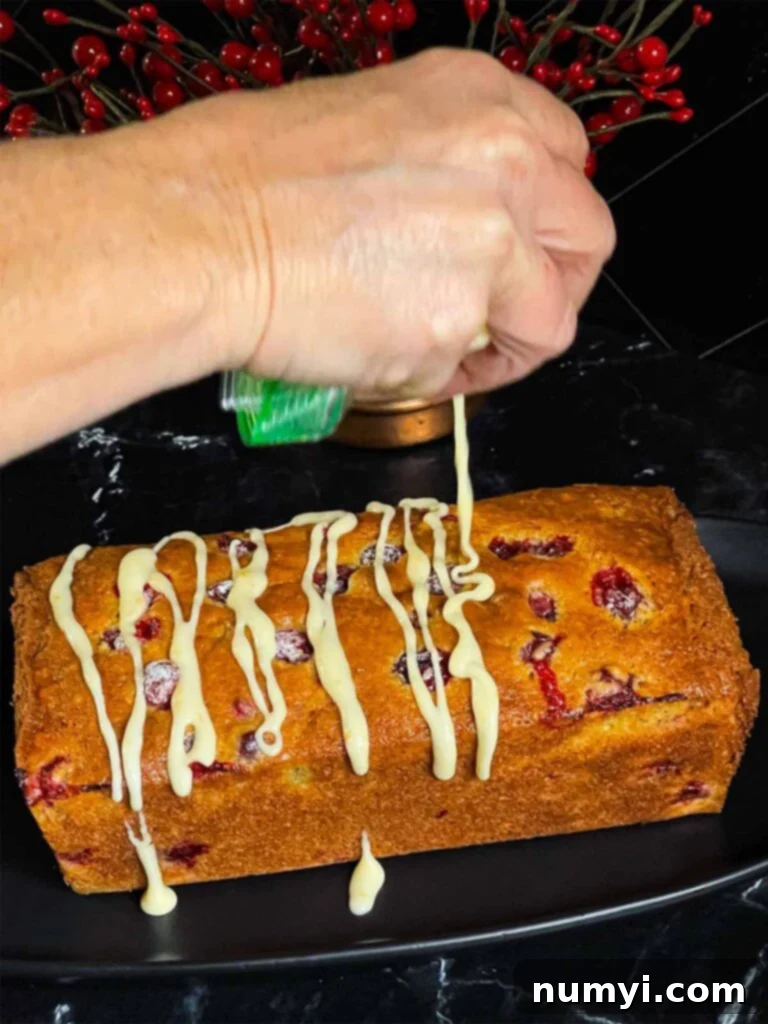 Zesty Cranberry Orange Loaf 13 Icing being drizzled onto a freshly baked loaf of Cranberry Orange bread.
