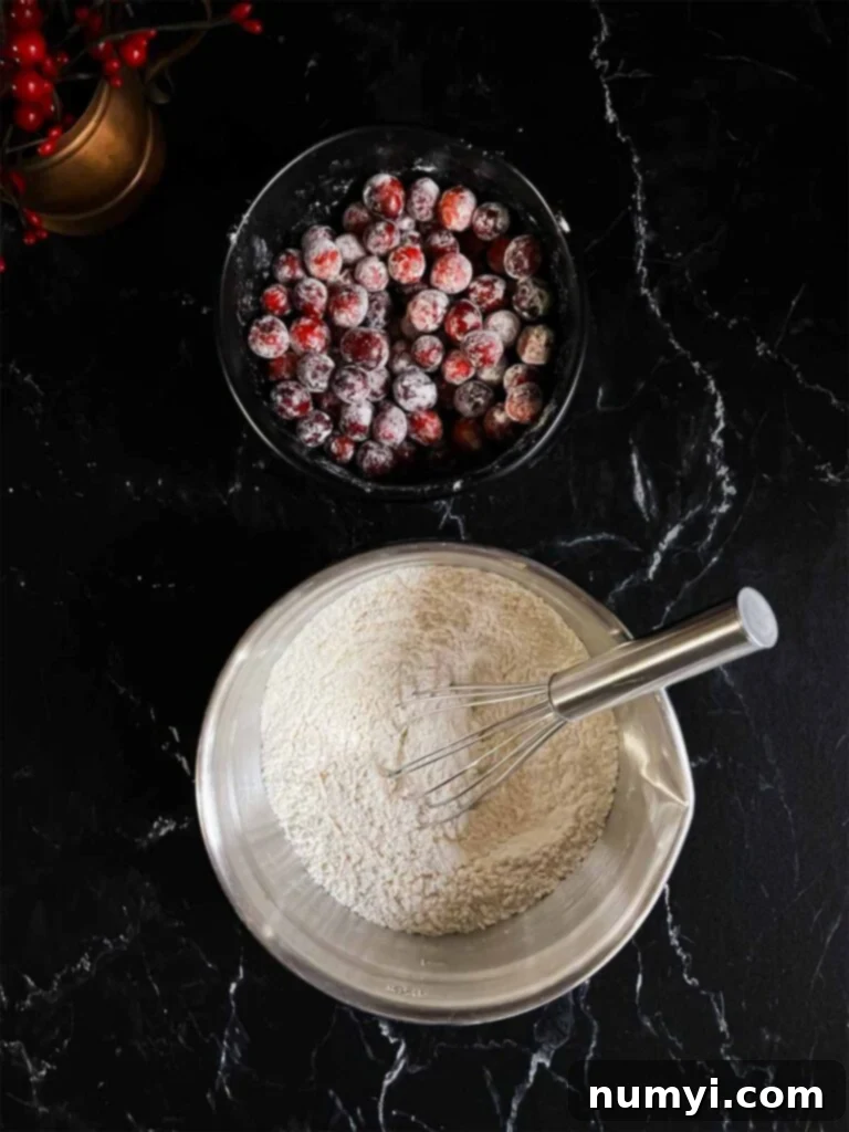 Zesty Cranberry Orange Loaf 5 A bowl of sugar dusted cranberries and a bowl of a flour mixture on a dark surface.