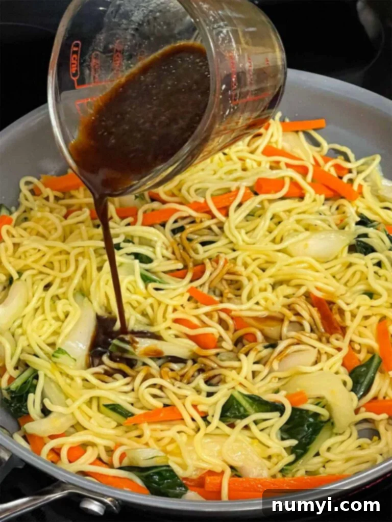 A rich, glossy Lo Mein sauce being poured over stir-fried noodles and vegetables in a hot skillet, ready to be mixed and absorbed, creating a harmonious blend of flavors and textures.