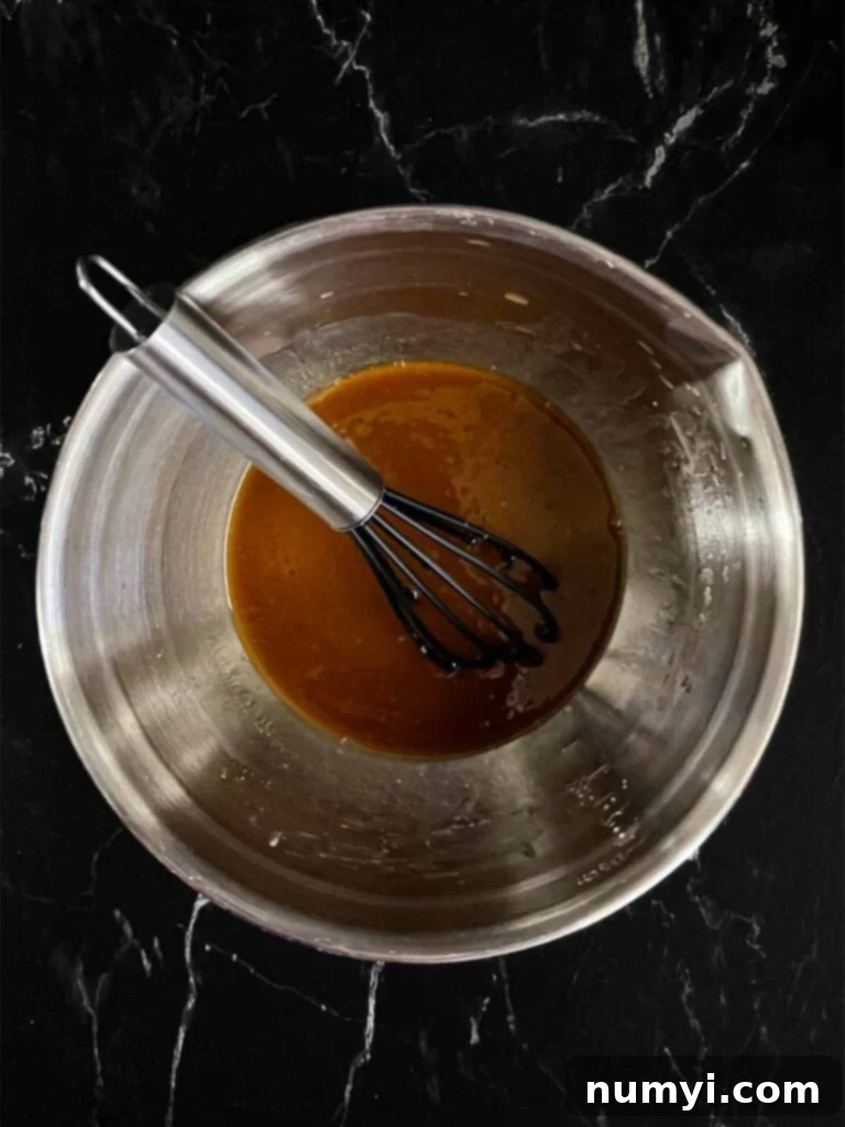 A mixing bowl filled with the prepared Lo Mein sauce, a rich brown liquid, sits on a dark surface, showcasing the simplicity and vibrancy of its key ingredients.
