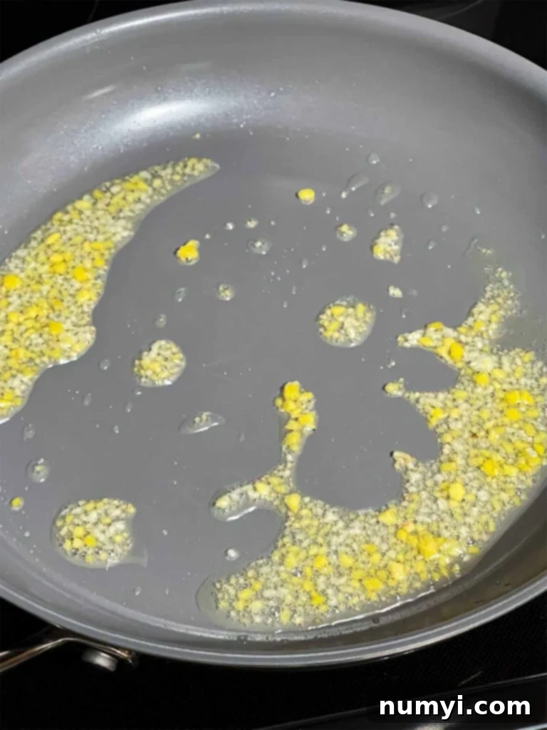 Finely diced garlic and ginger sizzling in hot vegetable oil in a stainless steel skillet, releasing a fragrant aroma and beginning to lightly brown, a crucial first step for building flavor in the lo mein.