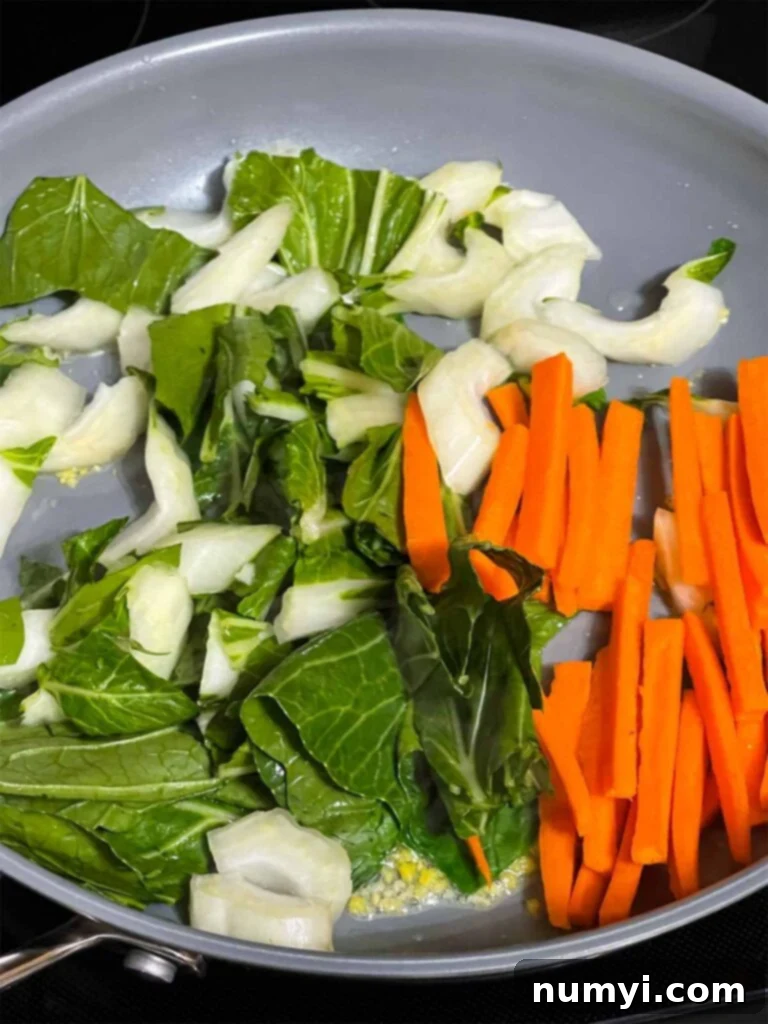 Freshly chopped bok choy and julienned carrots being stir-fried in a hot skillet with aromatic ginger and garlic, vibrant with color and retaining their crisp texture.