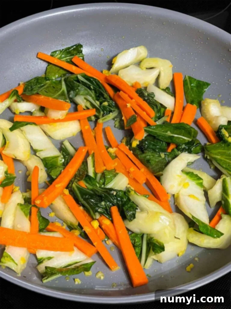 Vibrantly colored, tender-crisp bok choy and carrots, perfectly stir-fried and ready to mix with noodles, glistening with subtle oils and infused with aromatic spices in a skillet.