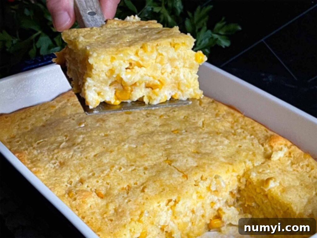 A golden-brown, creamy corn casserole serving being lifted from a baking pan, showing its perfect texture on a dark surface.