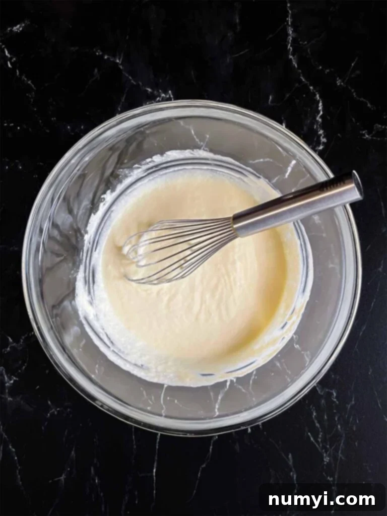 Wet ingredients for creamy corn casserole, including eggs, sour cream, and melted butter, whisked together smoothly in a glass mixing bowl.