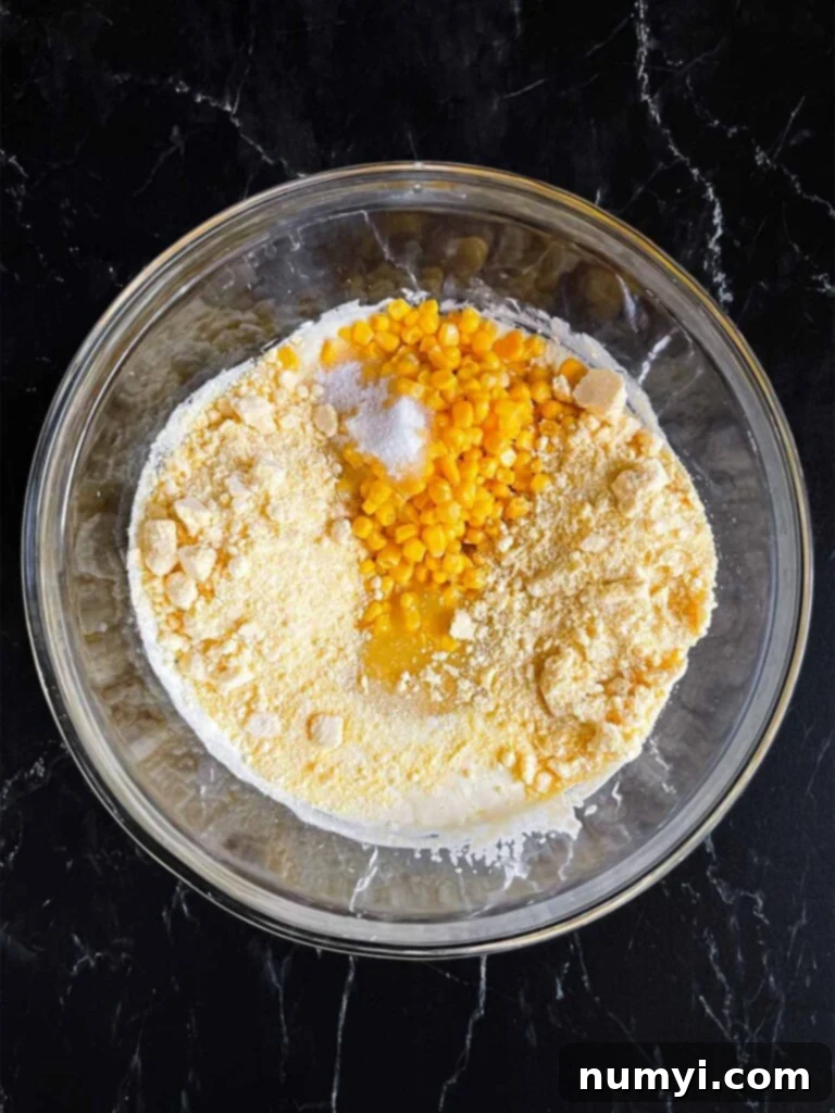 Wet ingredients mixed with canned corn and Jiffy mix in a glass bowl for creamy corn casserole.