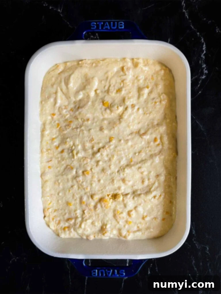 Creamy corn casserole batter poured into a baking pan, ready for the oven, on a dark surface.