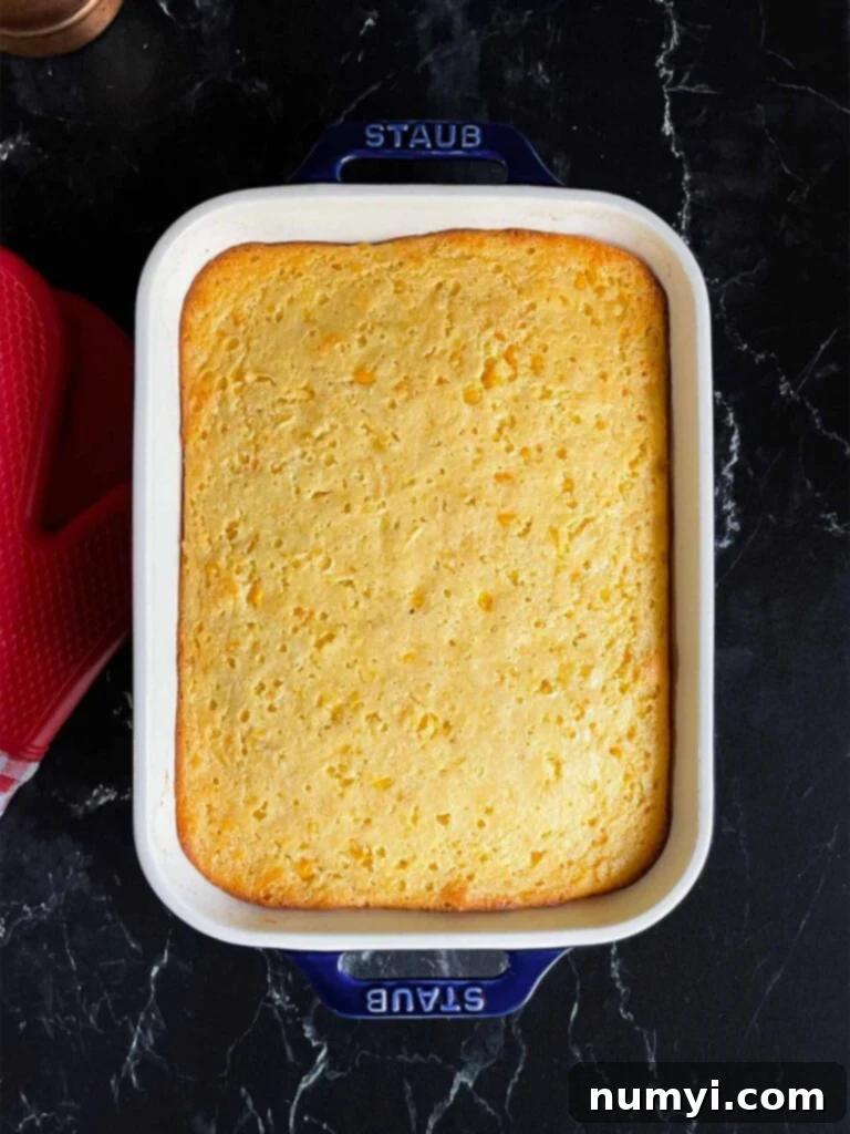 A perfectly baked, golden-brown creamy corn casserole in a pan, cooling on a dark surface.