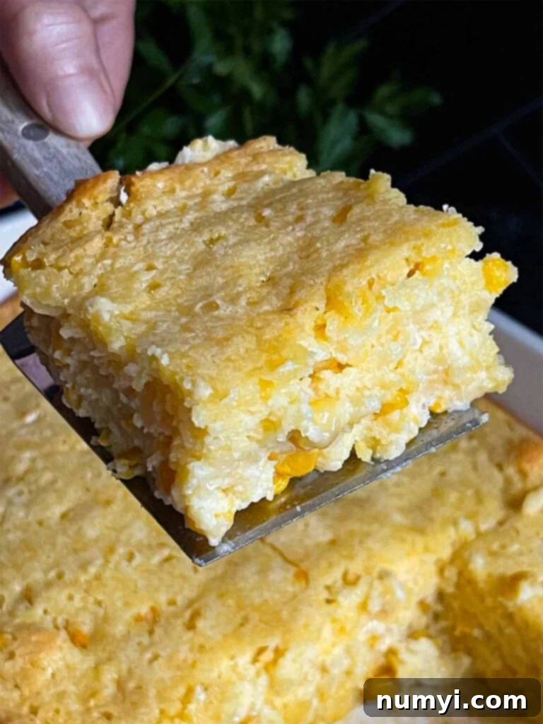 A serving of creamy corn casserole being scooped out of the baking pan with a spatula, highlighting its golden crust and creamy interior.