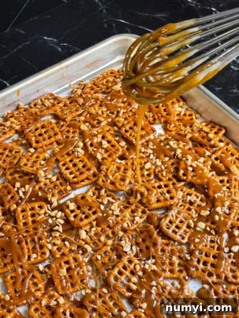 Hot butter toffee being carefully drizzled over pretzels laid out on a baking sheet, ensuring even coating.
