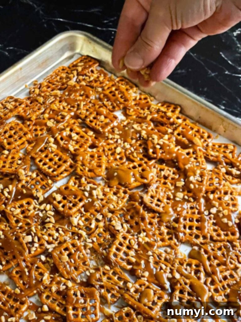 Toffee bits being sprinkled over warm, drizzled toffee on pretzels, adding extra texture and flavor.
