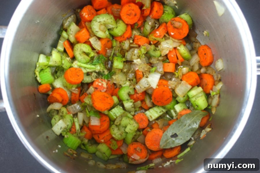 A vibrant mix of diced onions, carrots, and celery actively sautéing in a large pot, forming the aromatic base for the soup.
