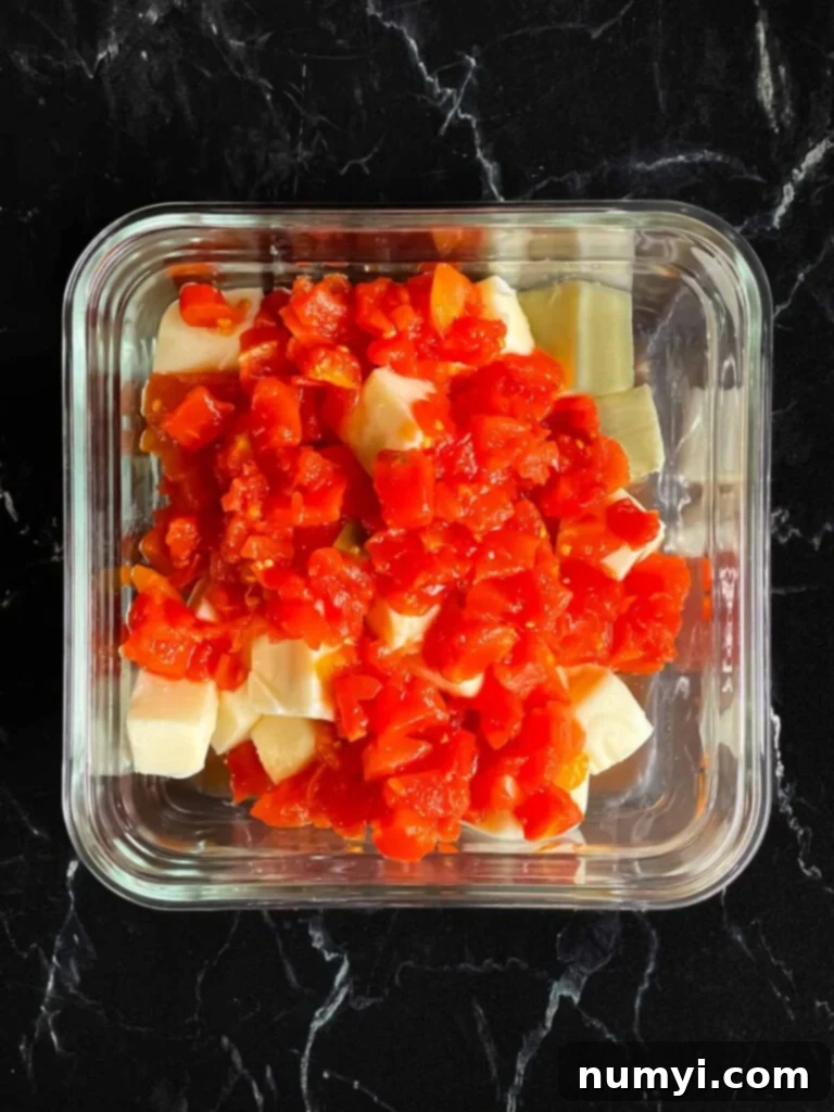 Cubed velveeta cheese with Rotel in a glass container.