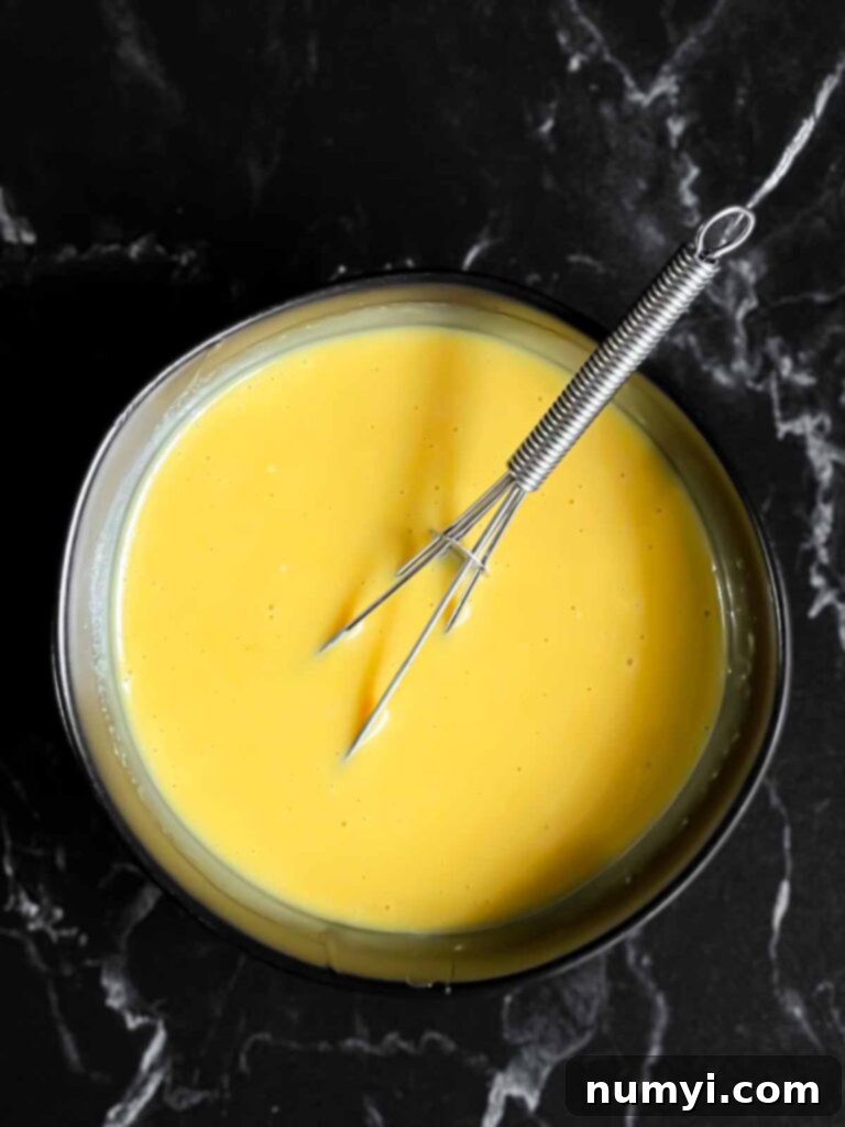 Honey mustard in a dark bowl with a whisk.
