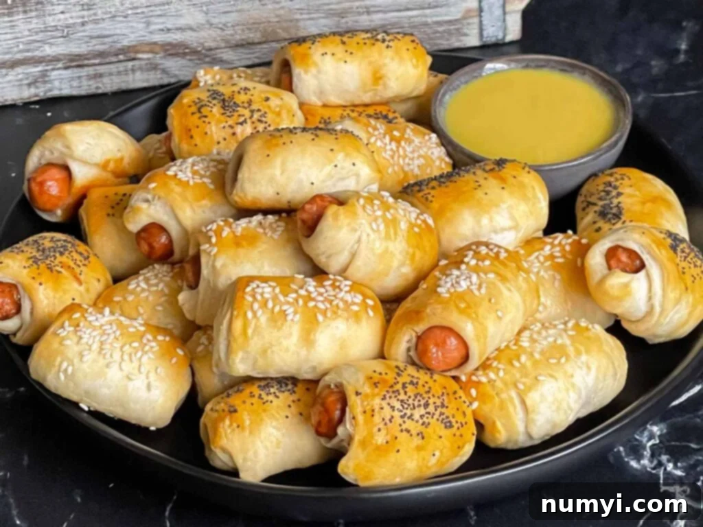 Fluffy Biscuit Pigs 2 Pigs in a blanket stacked on a dark plate with a ramekin of honey mustard sauce.