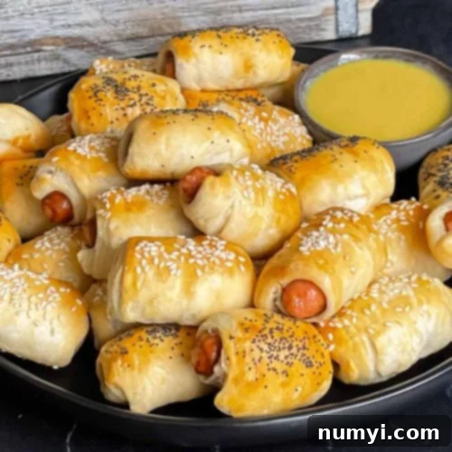 Fluffy Biscuit Pigs 9 Pigs in a blanket stacked on a dark plate with a ramekin of honey mustard sauce.