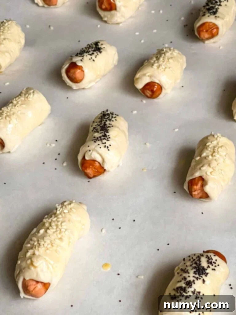 Fluffy Biscuit Pigs 7 Unbaked pigs in a blanket on a parchment paper lined baking sheet.