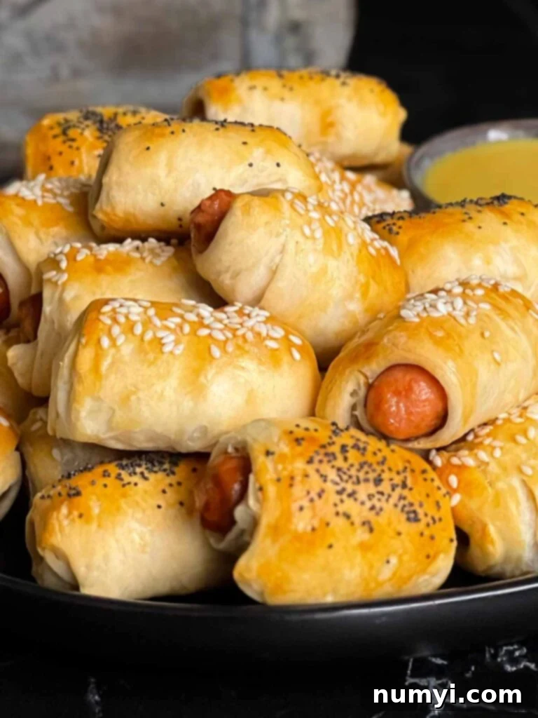 Fluffy Biscuit Pigs 8 Pigs in a blanket stacked on a dark plate with a ramekin of honey mustard sauce.