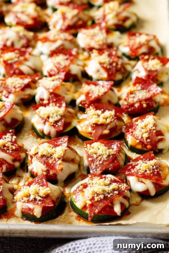 Close up of pizza bites on a baking sheet fresh from the oven, showcasing melted cheese and pepperoni on tender zucchini slices.